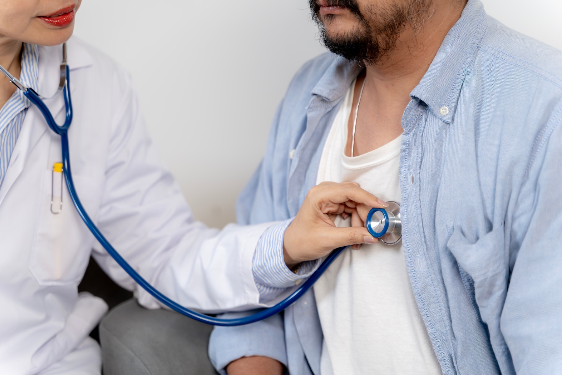 Female urgent care provider using stethoscope to check male patient's heartrate